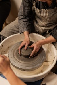 élève en train d'apprendre à tourner sur un tour de potier, les mains dans l'argile