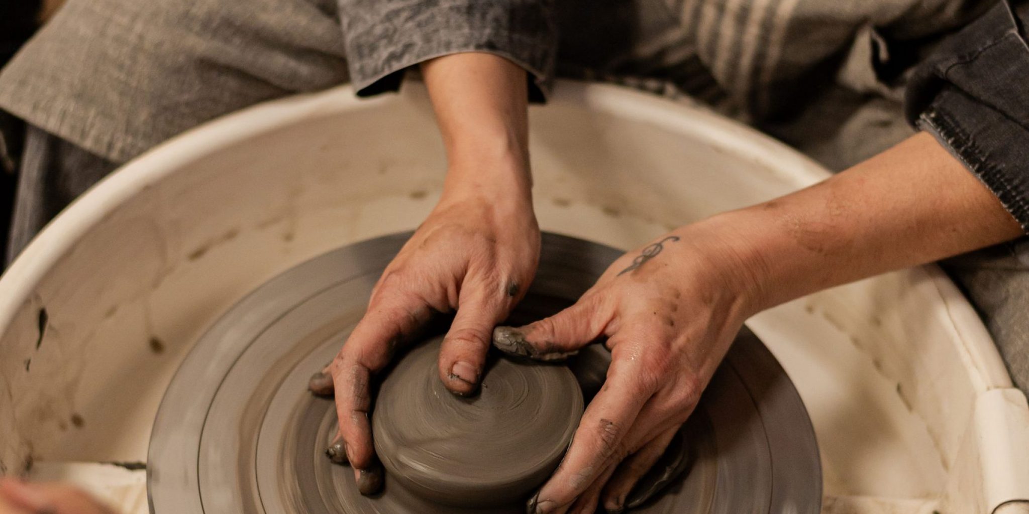 élève en train d'apprendre à tourner sur un tour de potier, les mains dans l'argile